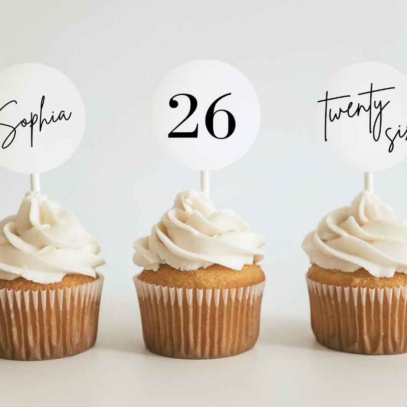 Three cupcakes with cupcake toppers that say "Sophia", "26", and "twenty six"